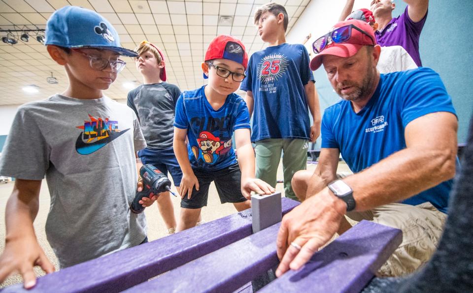 Under the direction of Scott Robinson, right, Logan Keller, center, holds a spacing block as Kory Lee, left, Lincoln Manning, second from left, and Isaac Eason, second front right, watch as they assemble buddy benches at Clear Creek Christian School on Friday, May 12, 2023.