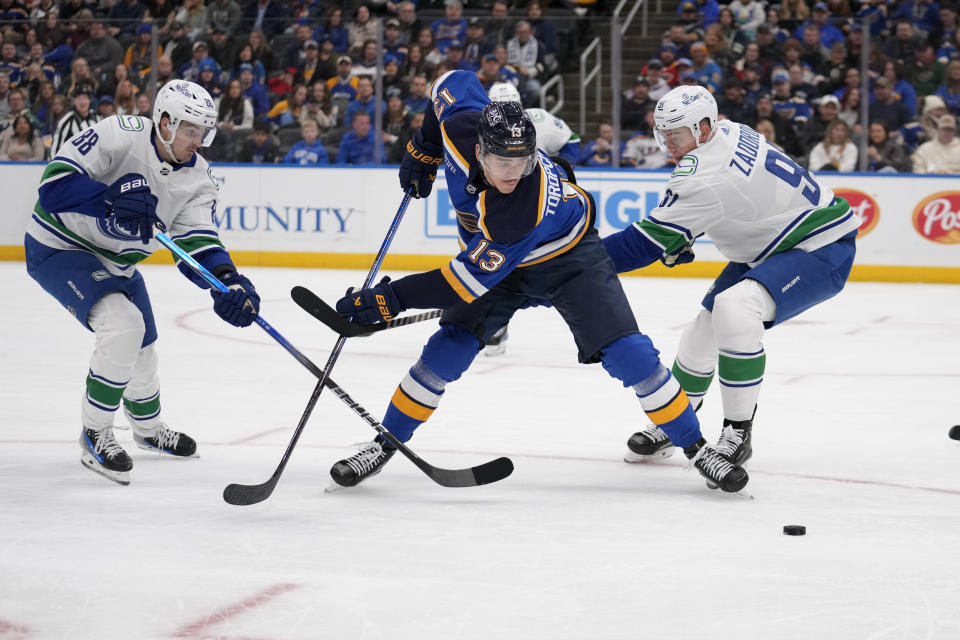 St. Louis Blues' Alexey Toropchenko (13) reaches for a loose puck as Vancouver Canucks' Nils Aman, left, and Nikita Zadorov, right, defend during the second period of an NHL hockey game Thursday, Jan. 4, 2024, in St. Louis. (AP Photo/Jeff Roberson)