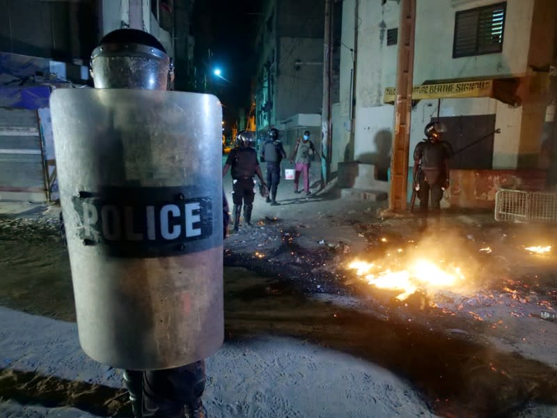 A riot police officer holds a shield while others try to put out a fire in the middle of the street during protests in Dakar