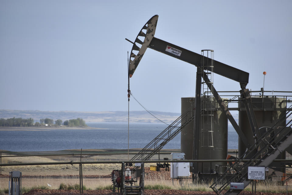 In this Wednesday, May 19, 2021, photo, a pump jack extracts oil from beneath the ground on the Fort Berthold Indian Reservation, with Lake Sakakawea in the background, east of New Town, North Dakota. About half of the 16,000 members live on the Fort Berthold Indian Reservation atop one of the biggest U.S. oil discoveries in decades. (AP Photo/Matthew Brown)