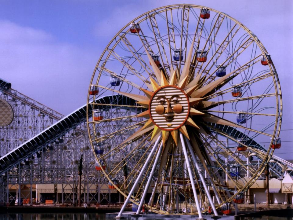 A large ferris wheel with a giant yellow sun with a face in the center and multiple gondala cars around the center and outside of the structure.