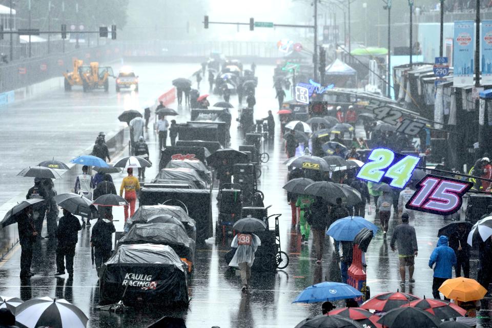 People walk along pit row in the rain before a NASCAR Cup Series auto race at the Grant Park 220 Sunday, July 2, 2023, in Chicago.