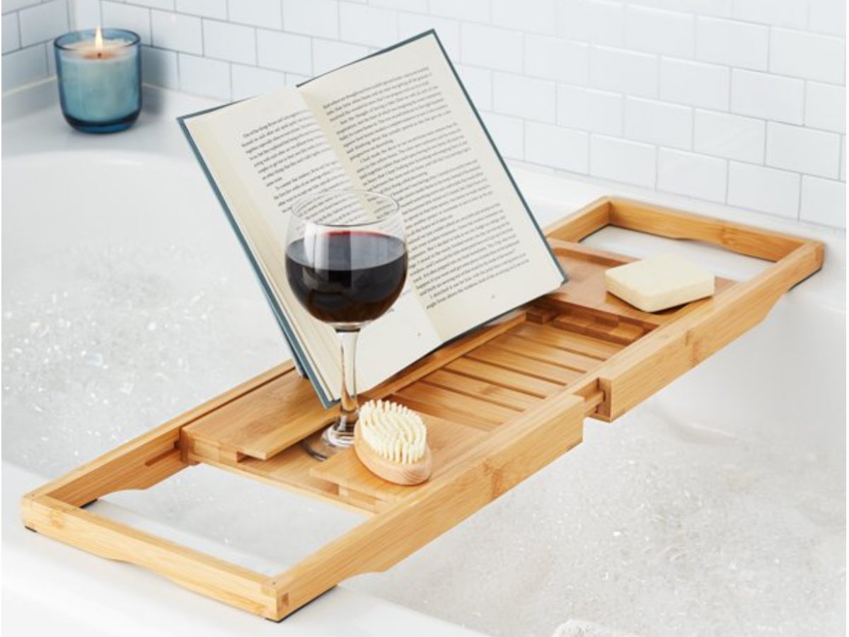 Bamboo tub caddy with wine glass, book and soap on it, over the tub