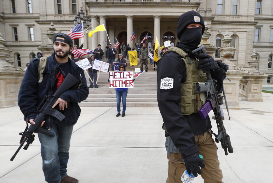 FILE - In this April 15, 2020, file photo, men carry rifles near the steps of the State Capitol building in Lansing, Mich., during a protest over Michigan Gov. Gretchen Whitmer's orders to keep people at home and businesses locked during the coronavirus outbreak.(AP Photo/Paul Sancya, File)