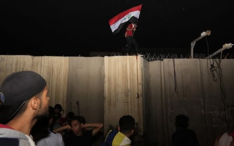 An Iraqi protester waves the Iraqi national flag as he stands on a concrete wall at the Iranian consulate in Karbala, Iraq - Credit: REX