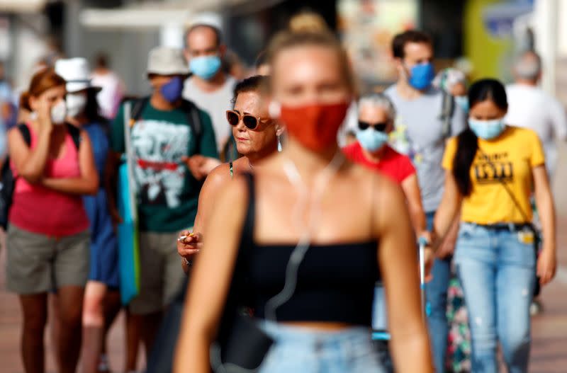 A woman smokes a cigarette while walking alongside other people wearing protective masks during the spread of the coronavirus disease (COVID-19) pandemic, in Las Palmas