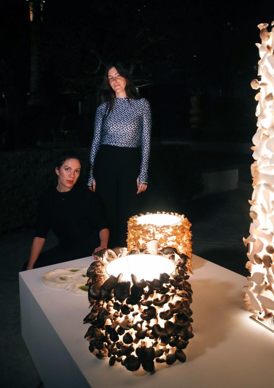 Two artists stand next to their mushroom lamps.