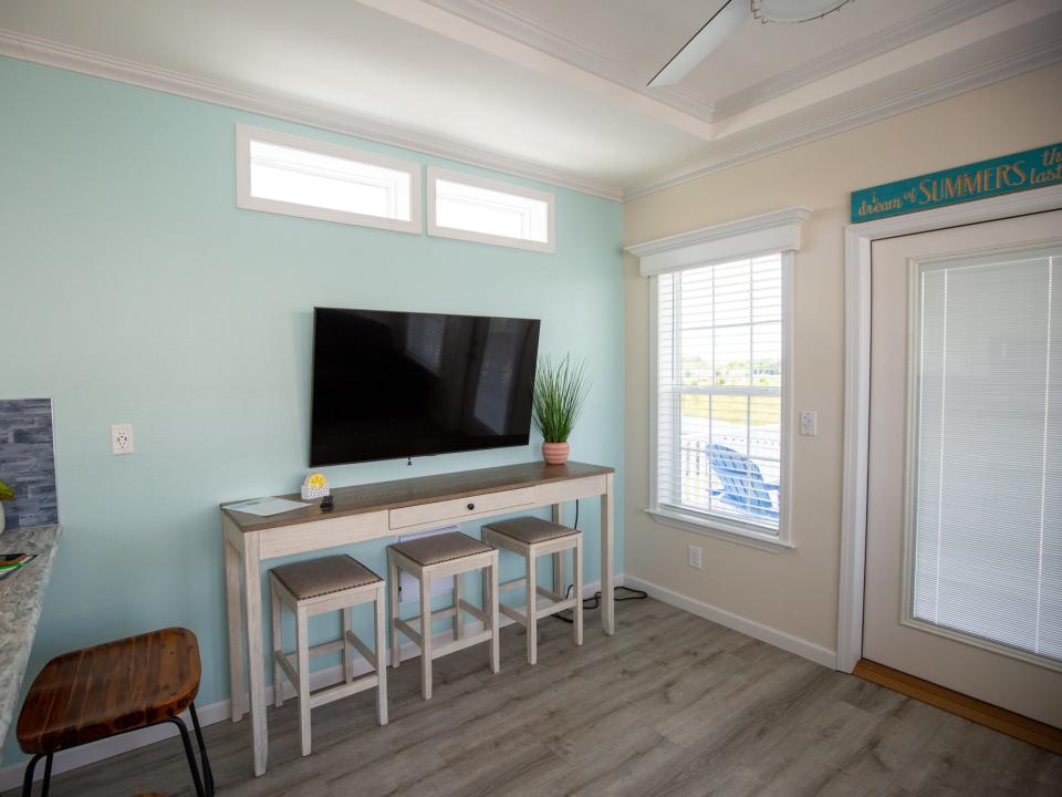 Inside a cabana cabin with windows, a TV, tables with chairs, and a door.