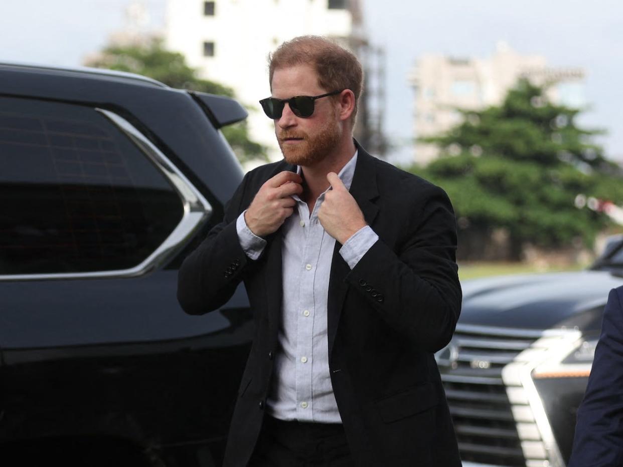 Prince Harry adjusts his collar as he exits a car.