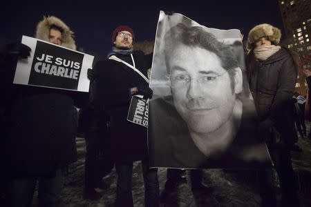 People hold a poster of Bernard Verlhac, a cartoonist known as Tignous, who was killed by gunmen at the offices of weekly satirical magazine Charlie Hebdo in Paris, during a vigil to pay tribute to the victims, in the Manhattan borough of New York, January 7, 2015. REUTERS/Carlo Allegri