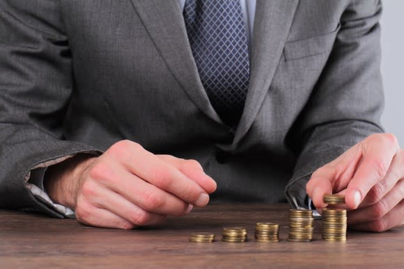 Man in suit stacking successively taller rows of coins