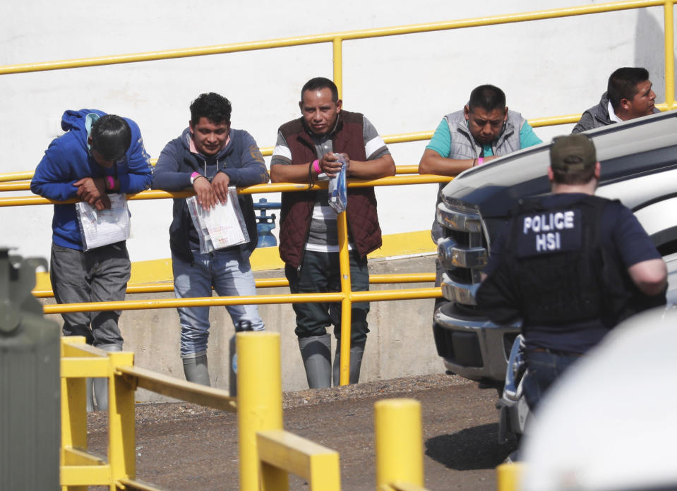 FILE - In this this Aug. 7, 2019, file photo, handcuffed workers await transportation to a processing center following a raid by U.S. immigration officials at Koch Foods Inc., plant in Morton, Miss. Federal officials announced Thursday, Aug. 6, 2020, the indictments of four executives from two Mississippi poultry processing plants on federal charges tied to one of the largest workplace immigration raids in the U.S. in the past decade. (AP Photo/Rogelio V. Solis, File)