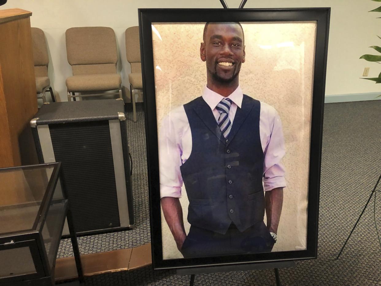 A portrait in a black frame of Tyre Nichols, looking upbeat in vest, tie and white shirt, is propped on the floor in front of some audio equipment and seating.