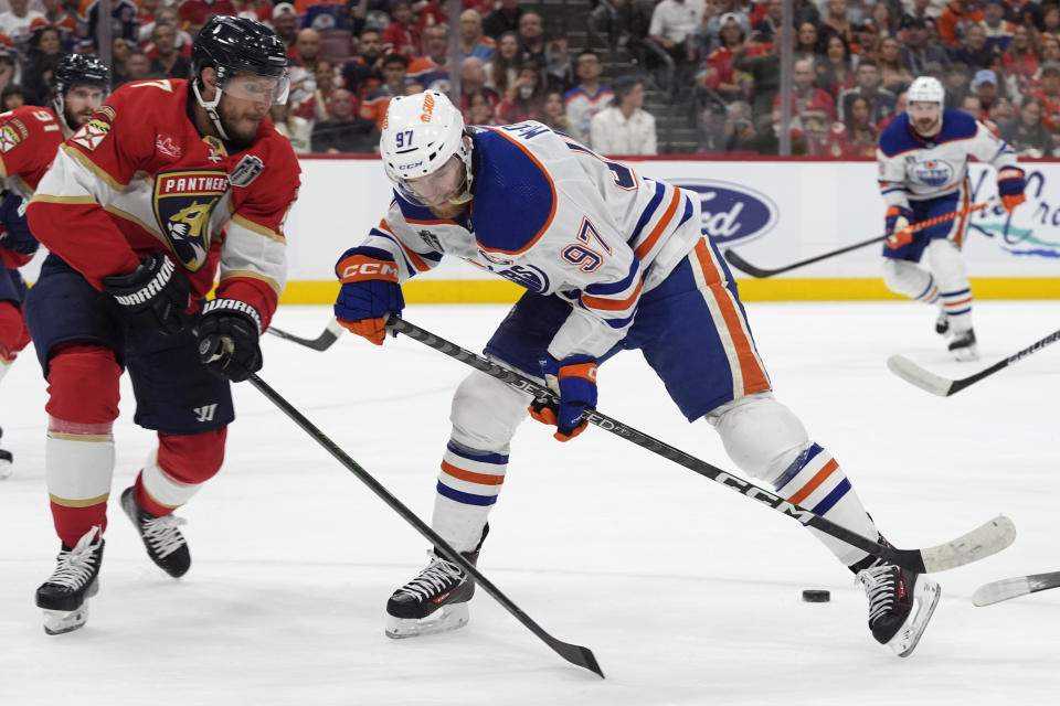 Florida Panthers defenseman Dmitry Kulikov (7) and Edmonton Oilers center Connor McDavid (97) go for the puck during the first period of Game 1 of the NHL hockey Stanley Cup Finals, Saturday, June 8, 2024, in Sunrise, Fla. (AP Photo/Wilfredo Lee)