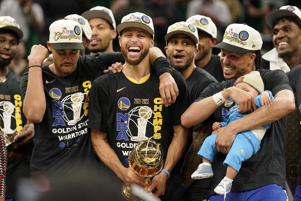 Golden State Warriors guard Stephen Curry, center, celebrates with teammates as he holds the Bill Russell Trophy for Most Valuable Player after the Warriors beat the Boston Celtics in Game 6 to win basketball's NBA Finals, Thursday, June 16, 2022, in Boston. (AP Photo/Steven Senne)