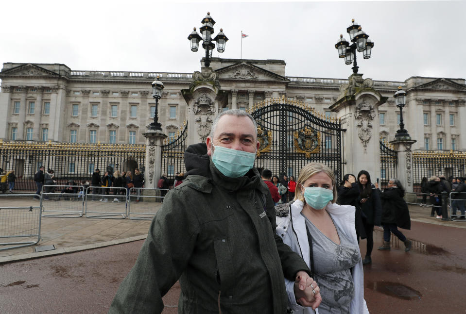 A couple wear face masks as they visit Buckingham Palace in London, Saturday, March 14, 2020. For most people, the new coronavirus causes only mild or moderate symptoms, such as fever and cough. For some, especially older adults and people with existing health problems, it can cause more severe illness, including pneumonia. (AP Photo/Frank Augstein)