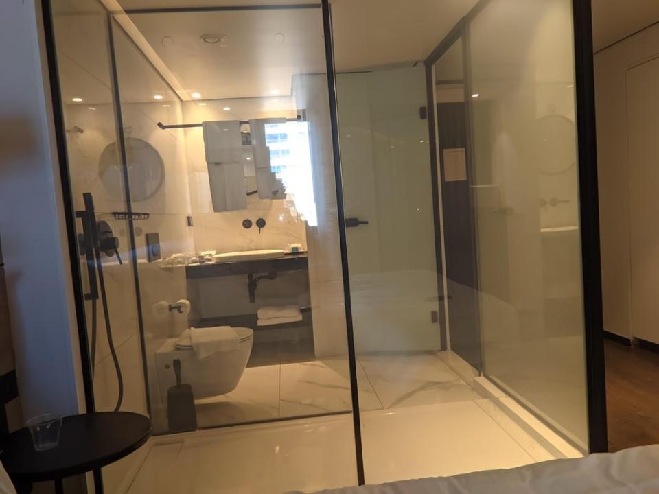 View of a hotel room's interior looking into a glass-walled bathroom with a visible toilet and shower