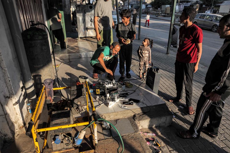 People gather around a charging station for cellphones, portable power supplies and car batteries connected to a fuel-based electric generator on the side of a street in Rafah in the southern Gaza Strip on Oct. 31, amid ongoing battles between Israel and the Palestinian Hamas movement.