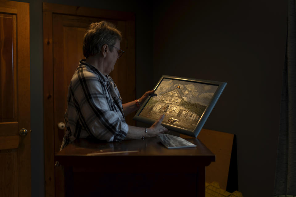 Kathy Miller holds a painting of the Elmore Store while sifting through mementos at her home Monday, March 4, 2024, in Elmore, Vt. Miller kept running the store for another 18 months before she was bought out by a community trust, set up to ensure the store remains open. These days, the store is run by Jason Clark. Miller helps out when she's not serving meals at a food kitchen. And she still collects her bills from P.O. Box 1. (AP Photo/David Goldman)