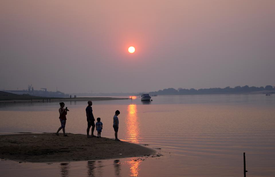 FILE - In this Aug. 21, 2021 file photo, a family is silhouetted against a reddish dusk caused by fires from the countryside, as they stand in the bay, connected to the Paraguay River in Asuncion, Paraguay. The water level hit a historic low on Sept. 23, 2021 amid a drought. (AP Photo/Jorge Saenz, File)