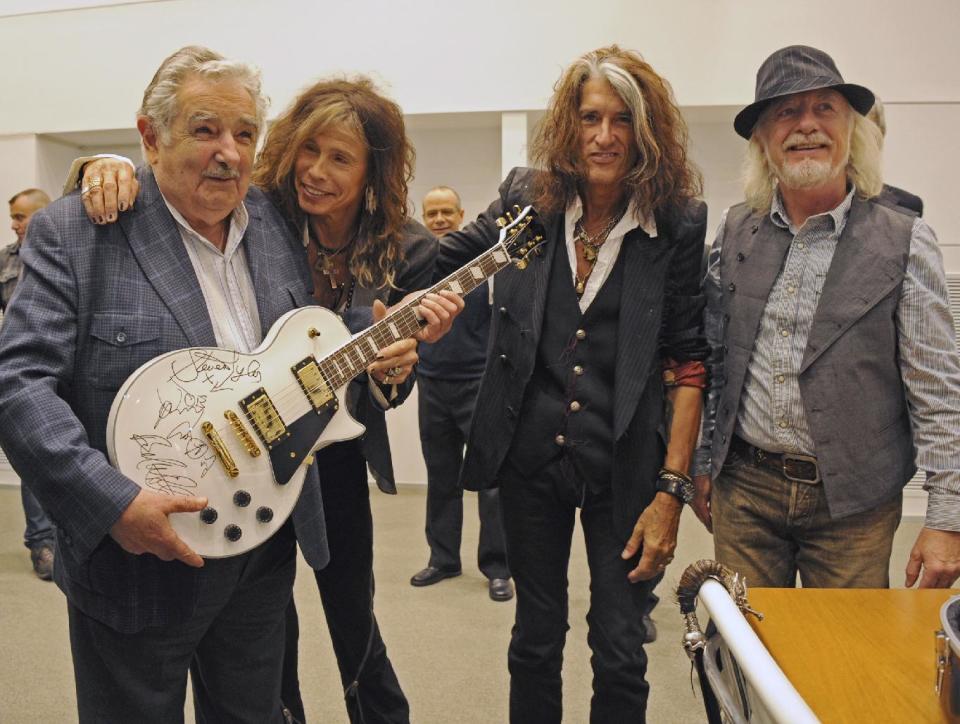 FILE - In this Oct. 8, 2013 file photo released by Uruguay's Press Office, President Jose Mujica, left, poses with Aerosmith's band members Steven Tyler, second from left, Joe Perry, second from right, and Brad Whitford after receiving an autographed guitar as a gift at presidential house in Montevideo, Uruguay. While outside his country he is an international figure, well known for his modest lifestyle, consistent with his ideals and his good-nature, among his own people Uruguay’s President known as "Pepe" does not generate such devotion and many question his management. (AP Photo/Uruguay Press Office, Alvaro Salas, File)