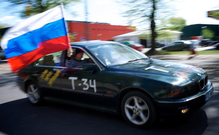 A man holds a Russian flag while passing by the World War II monument in Riga, on May 9, 2012, during Victory Day celebrations