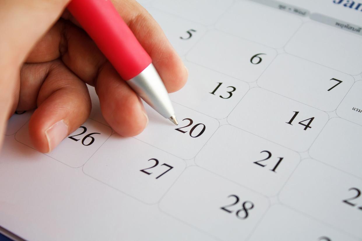 close-up of hand with pink pen looking at calendar