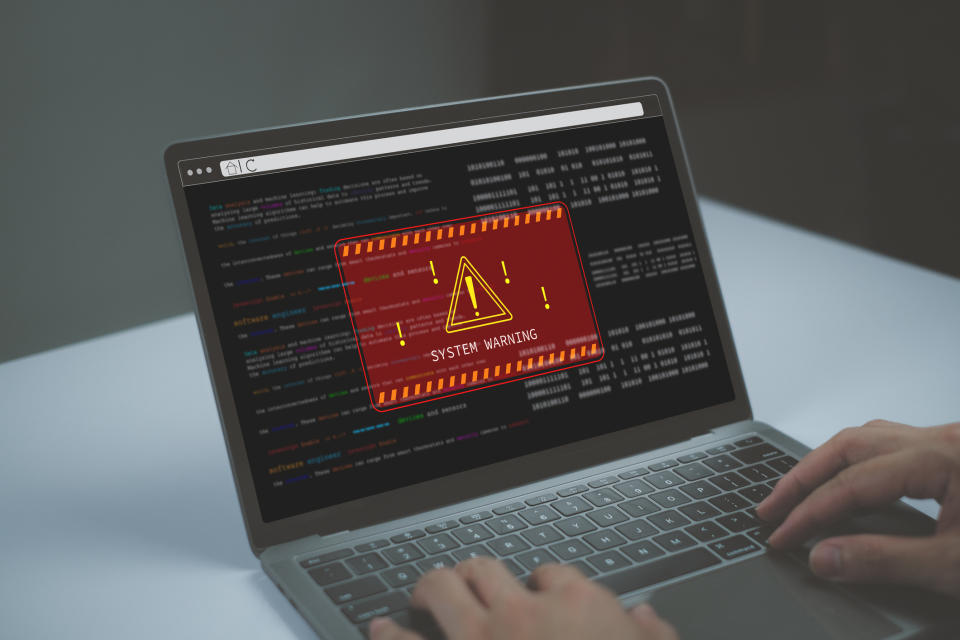 A person using a laptop with a system warning alert on the screen indicating an error