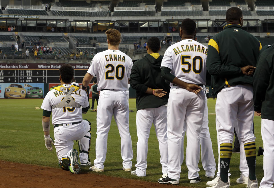 Oakland Athletics’ Mark Canha (20) places his hand on the shoulder of Bruce Maxwell as Maxwell kneels during the national anthem for the third consecutive day, prior to the team’s baseball game against the Seattle Mariners on Monday, Sept. 25, 2017, in Oakland, Calif. (AP Photo/Ben Margot)