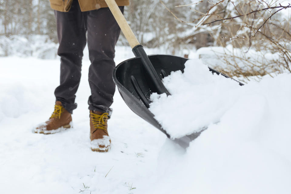 person in boots shovelling snow into a pile