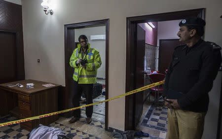 A member of the crime scene investigation unit looks at a policeman as he prepares to take photographs at a crime scene in Lahore January 13, 2015. REUTERS/Zohra Bensemra