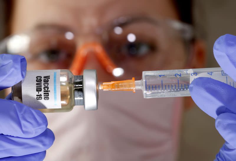 FILE PHOTO: A woman holds a small bottle labeled with a "Vaccine COVID-19" sticker and a medical syringe in this illustration