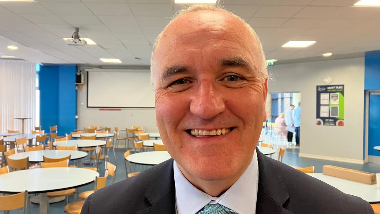 A smiling Michael Allen of Lisneal College is in the school's dining room, with tables and chairs in the background