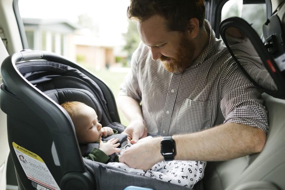 father buckling baby boy 2 3 months in car seat