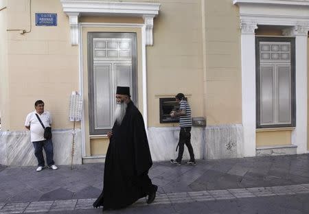 A Greek Orthodox priest walks past a bank branch as a man (R) makes a transactions at an ATM, in Athens September 20, 2013. REUTERS/John Kolesidis