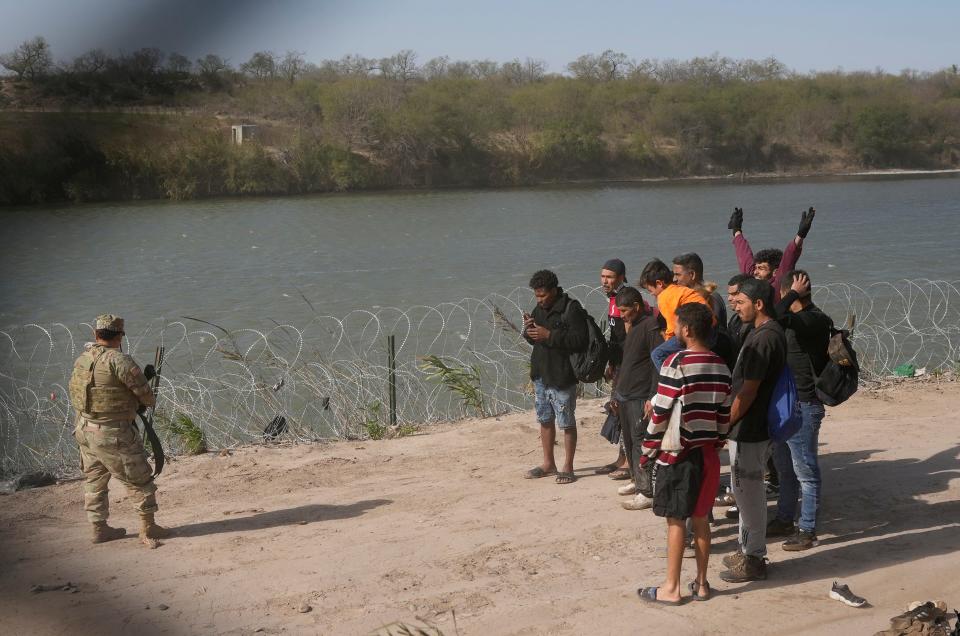 A group of migrants from Venezuela walk Monday along the Rio Grande in Eagle Pass to surrender to the Border Patrol. In a talk show interview, Gov. Greg Abbott said, "The only thing that we're not doing is we're not shooting people who come across the border, because, of course, the Biden administration would charge us with murder."