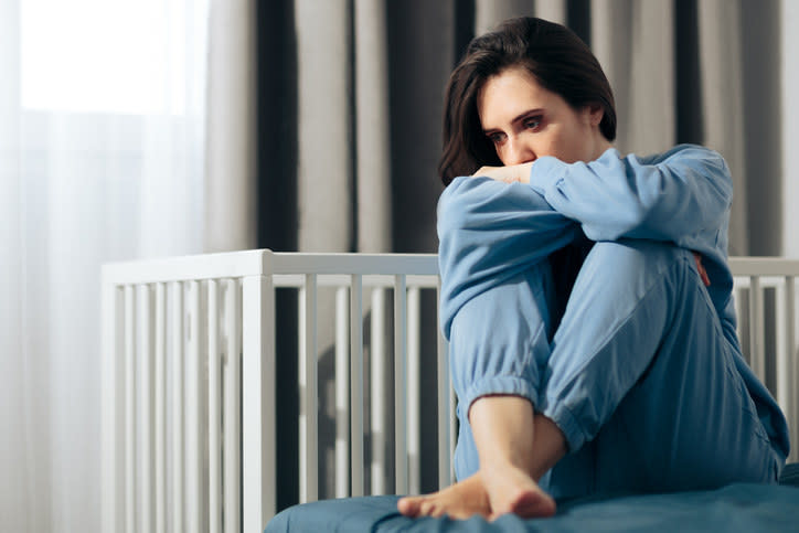 Woman looking sad next to an empty crib