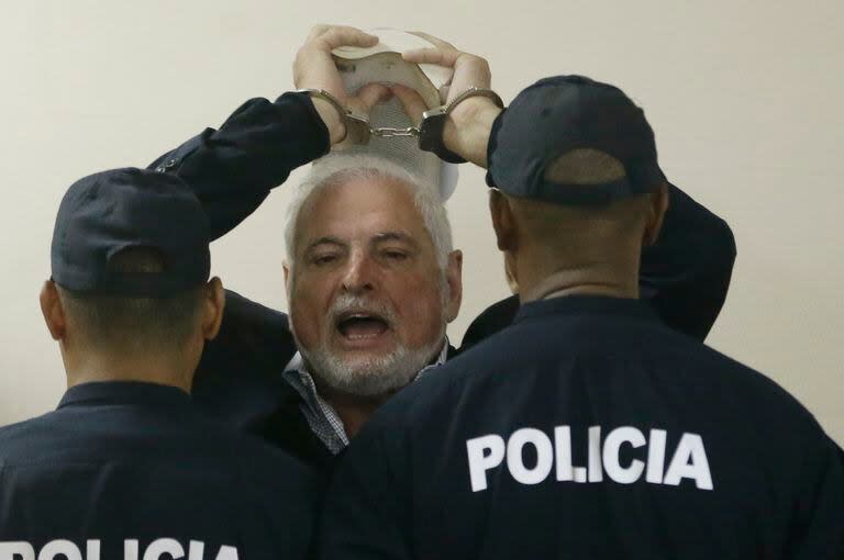 El expresidente de Panamá Ricardo Martinelli responde a los periodistas mientras levanta las manos esposadas y es escoltado por la policía a una audiencia en la Corte Suprema, el 19 de noviembre de 2018, en Panamá. (AP Foto/Arnulfo Franco, Archivo)