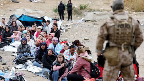 PHOTO: Immigrants seeking asylum in the U.S., who are stuck in a makeshift camp between border walls between the U.S. and Mexico, sit as a Customs and Border Protection officer keeps watch on May 13, 2023 in San Diego. (Mario Tama/Getty Images, FILE)