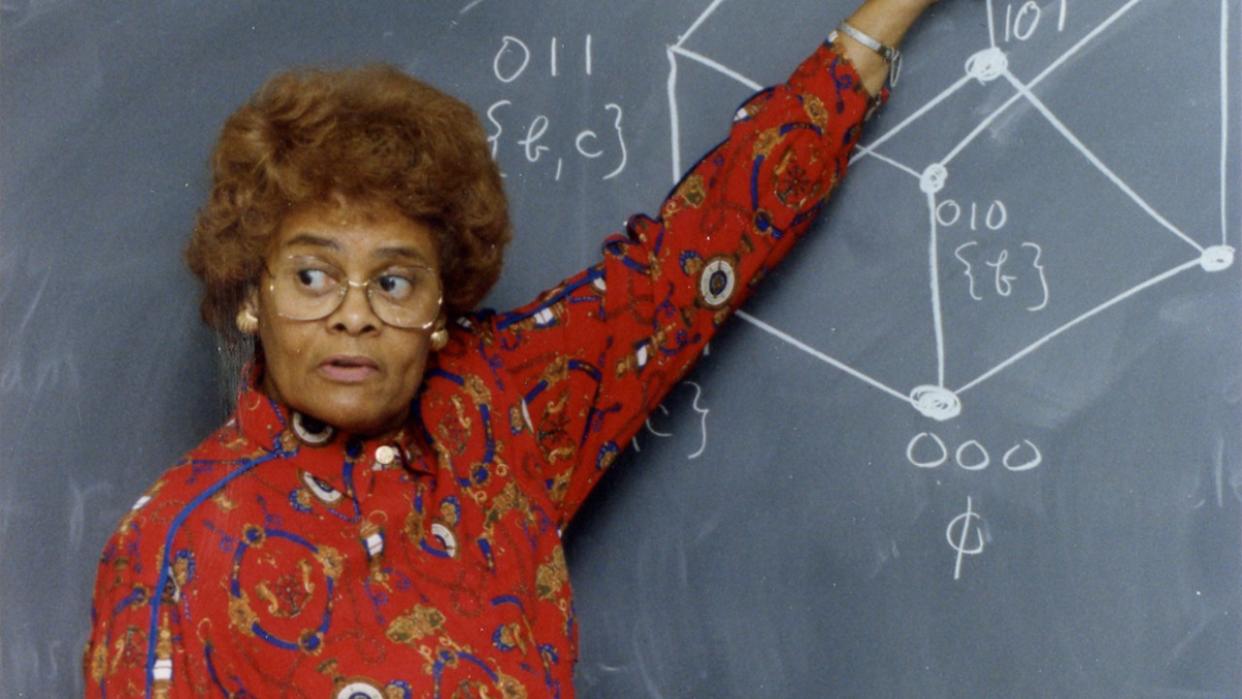  a woman points at a chalkboard containing math formulas 