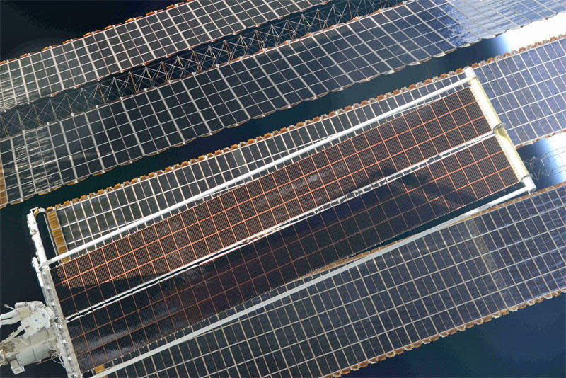 The new iROSA solar blanket, seen fully extended from the space station's left-side P6 solar array truss segment, in a shot by cosmonaut Oleg Novitskiy. Spacewalkers Thomas Pesquet and Shane Kimbrough are visible at lower left. / Credit: Oleg Novitskiy via NASA