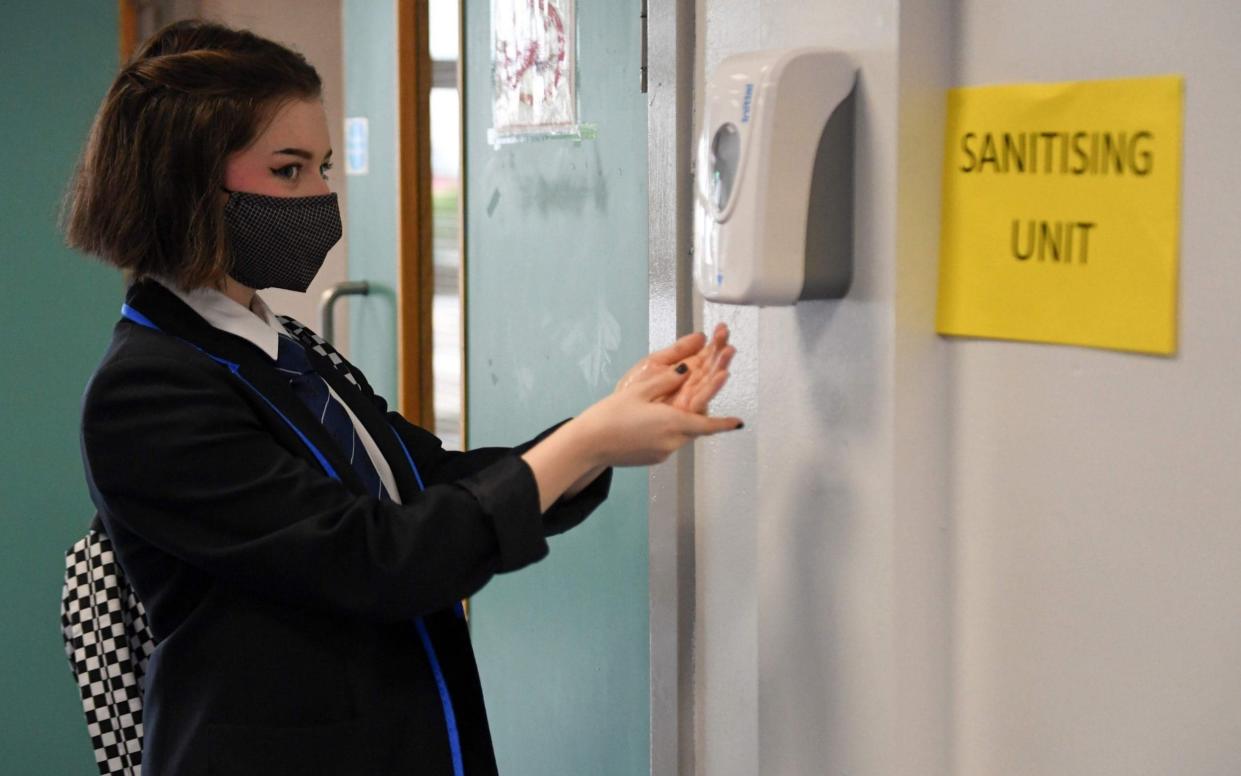 A secondary school pupil wearing a face mask sanitises her hands ahead of a lesson - Andy Buchanan/AFP