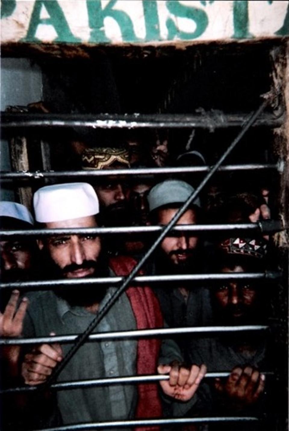 A group of bearded men stand behind a barred door.