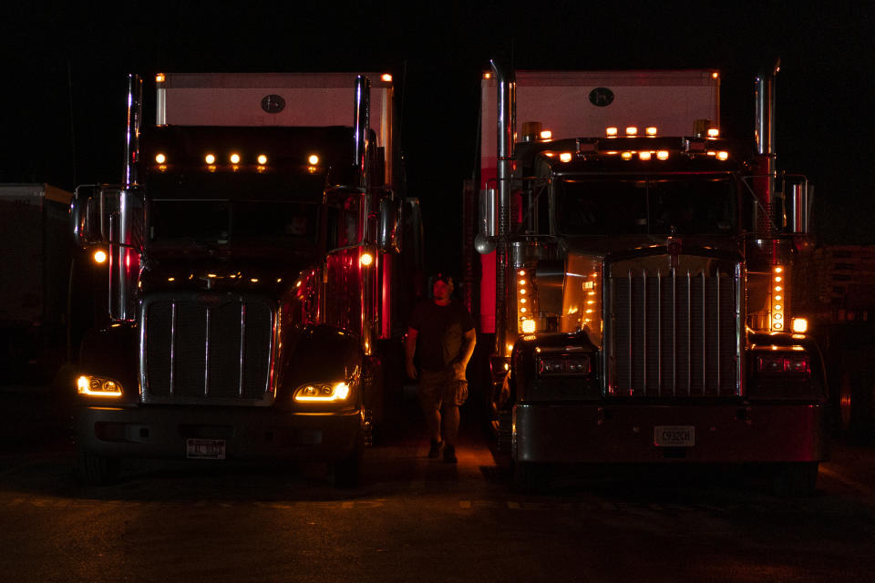 In this April 5, 2020, photo, professional driver Sammy Lloyd, of Ringgold, Ga., walks from his 2014 Kenworth W900 semi truck, on the right, as he arrives at the TA Travel Center truck stop in Foristell, Mo., just after midnight. Lloyd was pulling a COVID-19 emergency relief load from California to Virginia. (AP Photo/Carolyn Kaster)