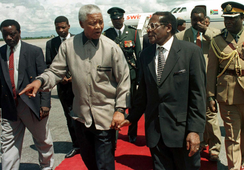 FILE - In this Sunday, Dec. 13, 1998 file photo, former South African president Nelson Mandela, left, walks with Zimbabwean President Robert Mugabe in Harare. Mugabe, the longtime leader of Zimbabwe who was forced to resign in 2017 after a military takeover, has died at 95. (AP Photo/Rob Cooper, File)