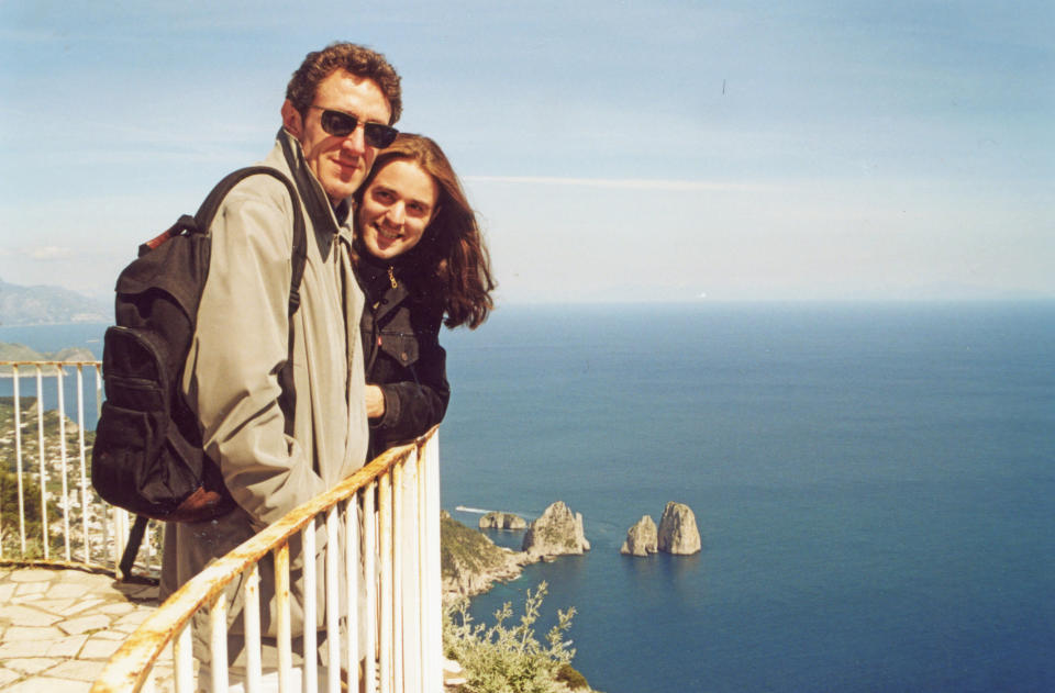 Two people embracing and smiling at the camera with a scenic ocean and sky backdrop