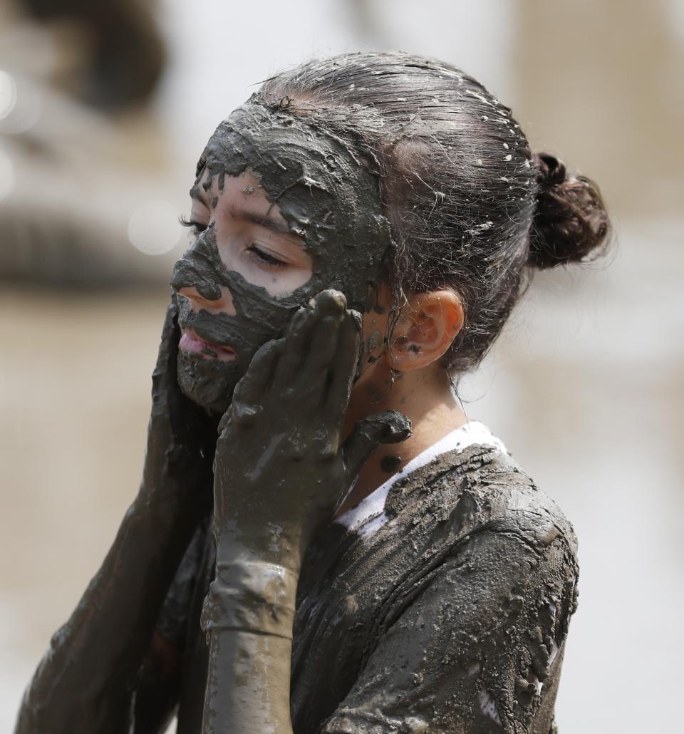 Tmiamelia Harris, 11, applies mud to her face during Mud Day at the Nankin Mills Park, Tuesday, July 9, 2019, in Westland, Mich. The annual day is for kids 12 years old and younger. While parents might be welcome, this isn't an event meant for teens or adults. It's all about the kids having some good, unclean fun during their summer break and is sponsored by the Wayne County Parks. (AP Photo/Carlos Osorio)