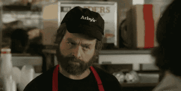 A man with a beard wearing an Arby's cap and apron looks with a perplexed expression in a kitchen setting