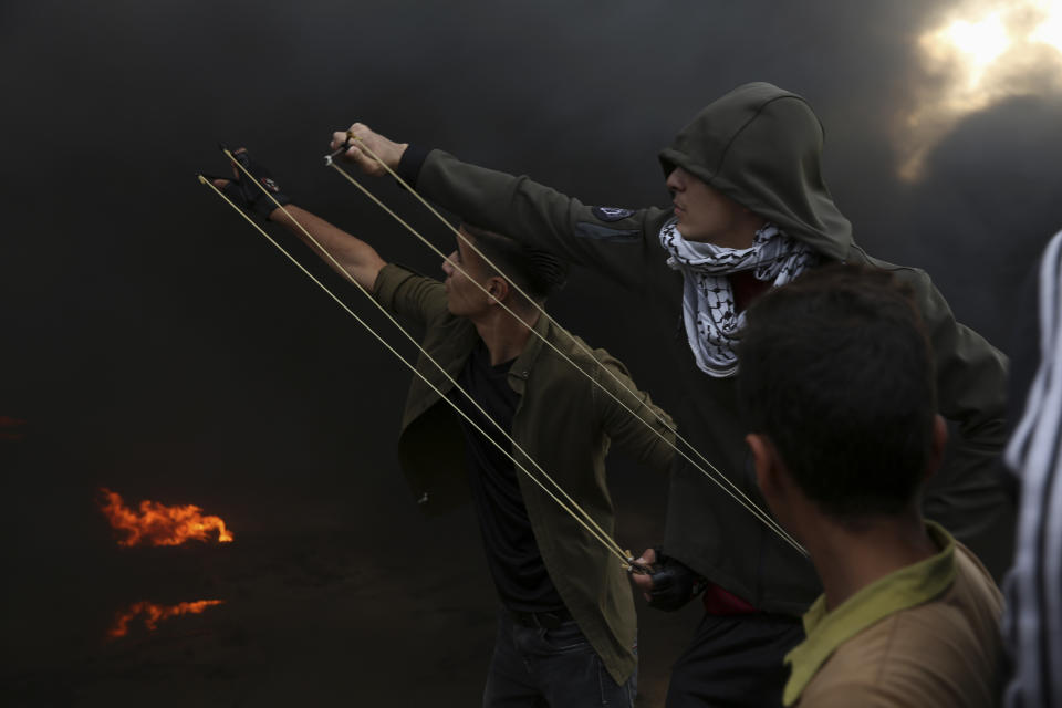 Protesters use sling shots to hurl stones at Israeli troops while others burn tires near the fence of the Gaza Strip border with Israel during a protest east of Gaza City, Friday, Oct. 26, 2018. (AP Photo/Adel Hana)