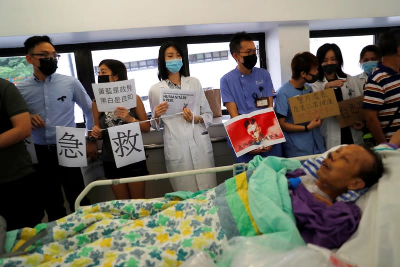 A patient is wheeled past as healthcare staff hold posters and participate in a human chain to protest against what they say is police brutality during the anti-extradition bill protests, at Queen Mary Hospital, in Hong Kong